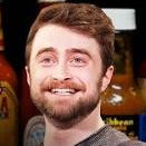 A man with a beard and brown hair is shown smiling in front of several hot sauce bottles, with a 'HOT ONES' graphic overlay on the bottom left.
